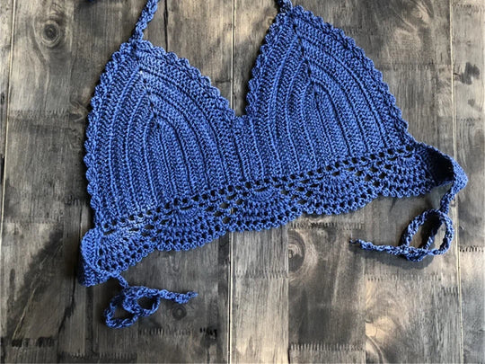 Haut de maillot de bain crochet tricoté bleu posé à plat sur du bois foncé, bretelles longues et bordure festonnée