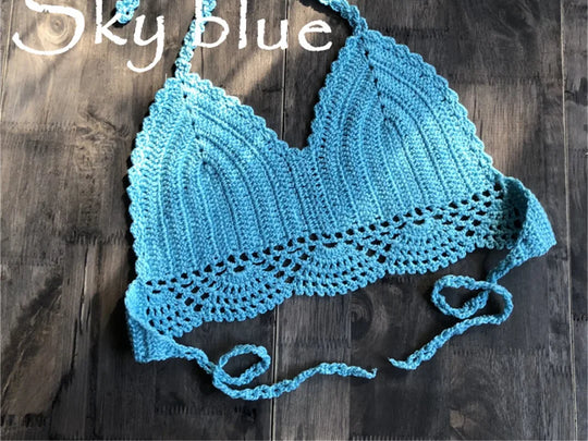 Haut de maillot de bain crochet tricoté bleu ciel posé à plat sur du bois foncé, bretelles longues et bordure festonnée