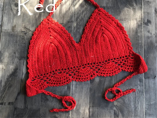 Haut de maillot de bain crochet tricoté rouge posé à plat sur du bois foncé, bretelles longues et bordure festonnée