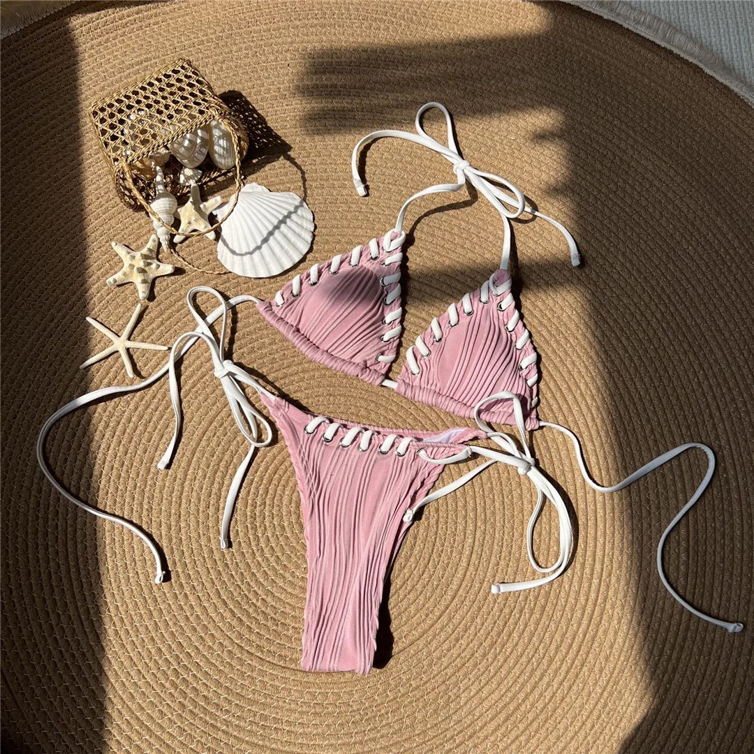 Bikini tour de cou rose à liserés blancs posé à plat sur une natte ronde, coquillages et étoiles de mer