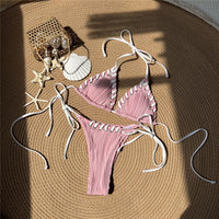 Bikini tour de cou rose à liserés blancs posé à plat sur une natte ronde, coquillages et étoiles de mer