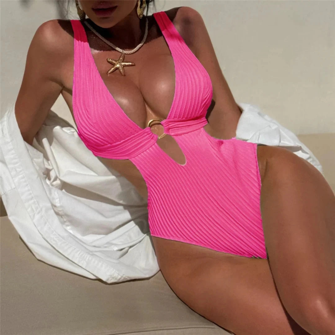 Maillot de bain une pièce décolleté plongeant à découpes rose fuchsia porté par une femme assise, anneau doré
