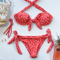 Bikini orange à pois posé à plat sur fond blanc, avec haut à nœud central et lacets latéraux du bas