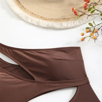 Gros plan sur la ceinture d'un maillot une pièce marron à découpe asymétrique, posé à plat sur fond blanc