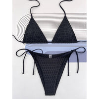 Bikini brésilien tour de cou noir texturé à plat sur un fond blanc rayé, bretelles fines et bas à liens noués