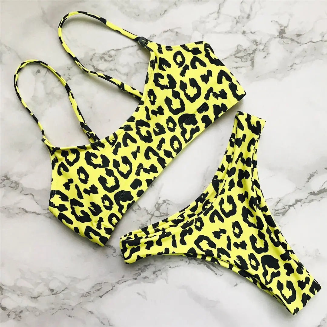 Bikini triangle brésilien à bretelles réglables jaune posé à plat sur marbre blanc, haut à bretelles fines et bas assorti à motifs noirs