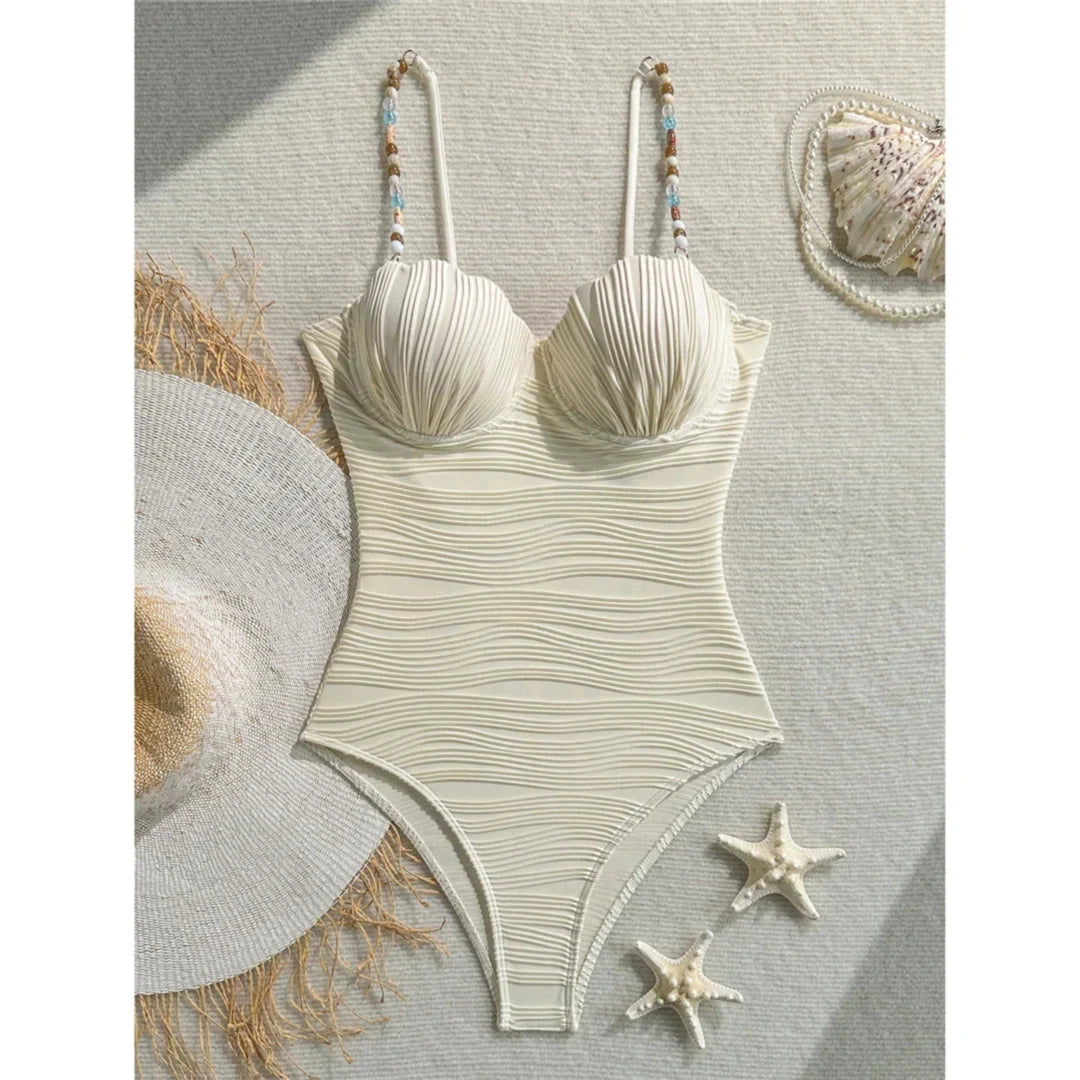 Maillot de bain une pièce à armatures beige posé à plat sur un tissu clair avec un chapeau de paille et des étoiles de mer