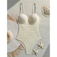 Maillot de bain une pièce à armatures beige posé à plat sur un tissu clair avec un chapeau de paille et des étoiles de mer