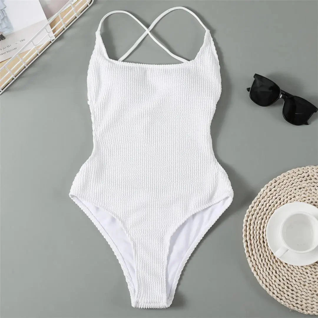 Maillot une pièce côtelé dos nu échancré blanc posé à plat sur fond gris, dos croisé, lunettes noires et chapeau à côté