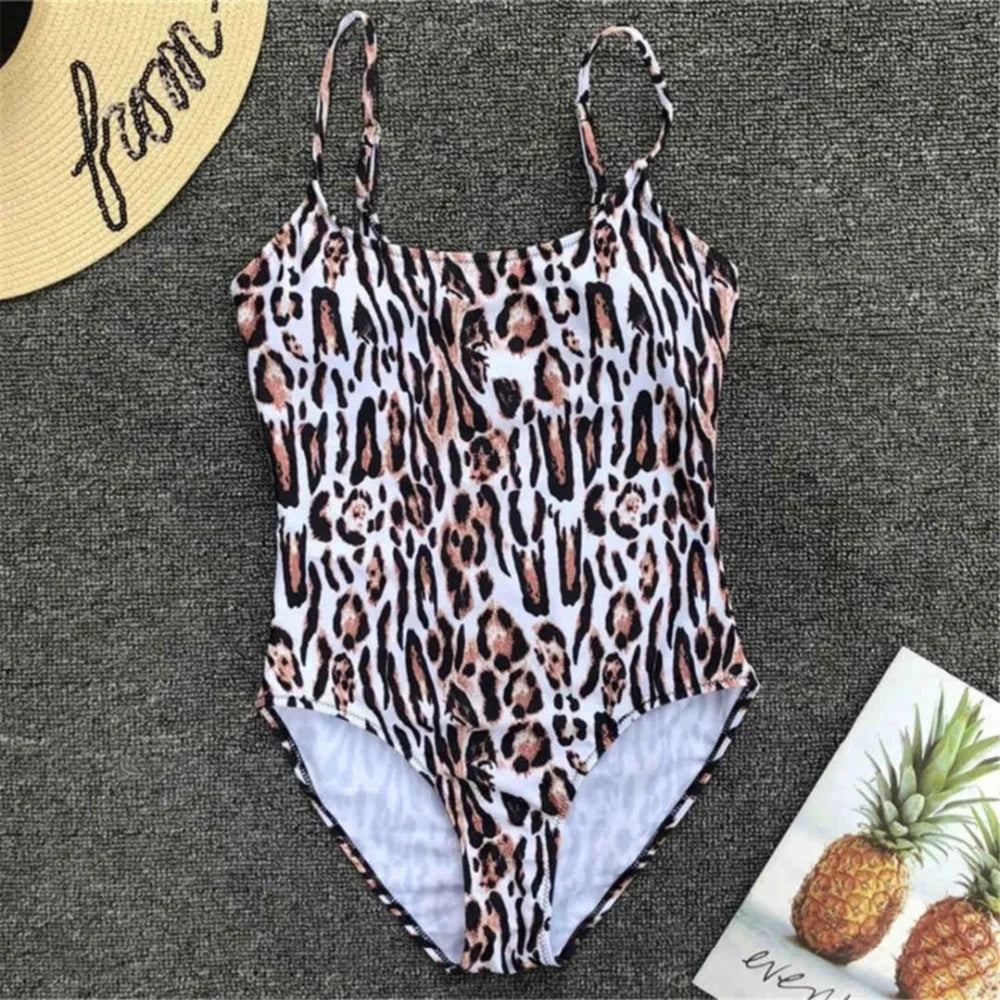Maillot une pièce triangle imprimé léopard sur fond clair posé à plat, bretelles fines, chapeau de paille et ananas à côté