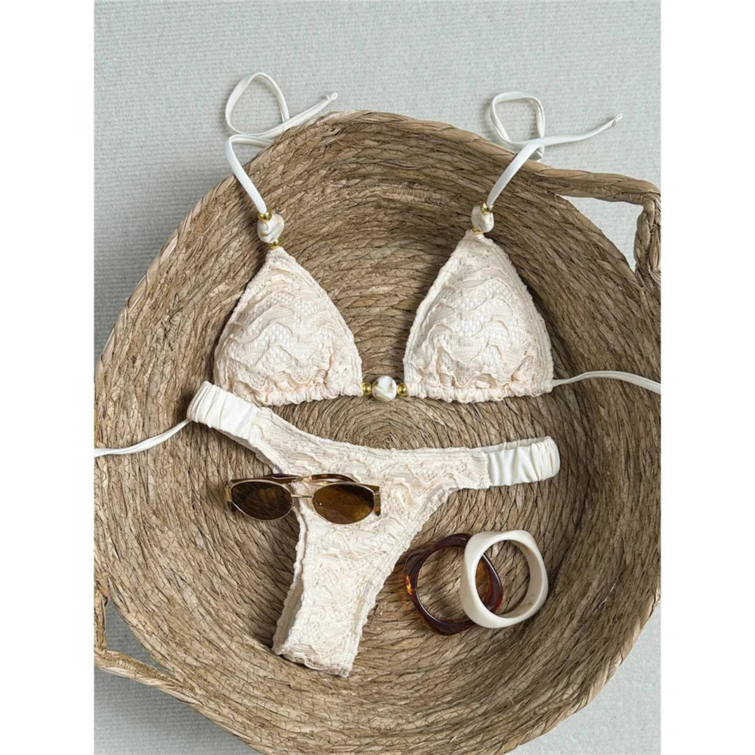 Bikini tour de cou effet froissé beige posé à plat sur un panier en osier, liens fins et perle dorée au centre du triangle