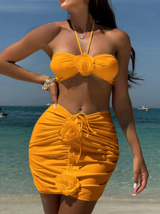 Maillot de bain trois pièces jupe fleurs en relief jaune porté de face sur la plage, bustier à fleur et jupe froncée à fleurs
