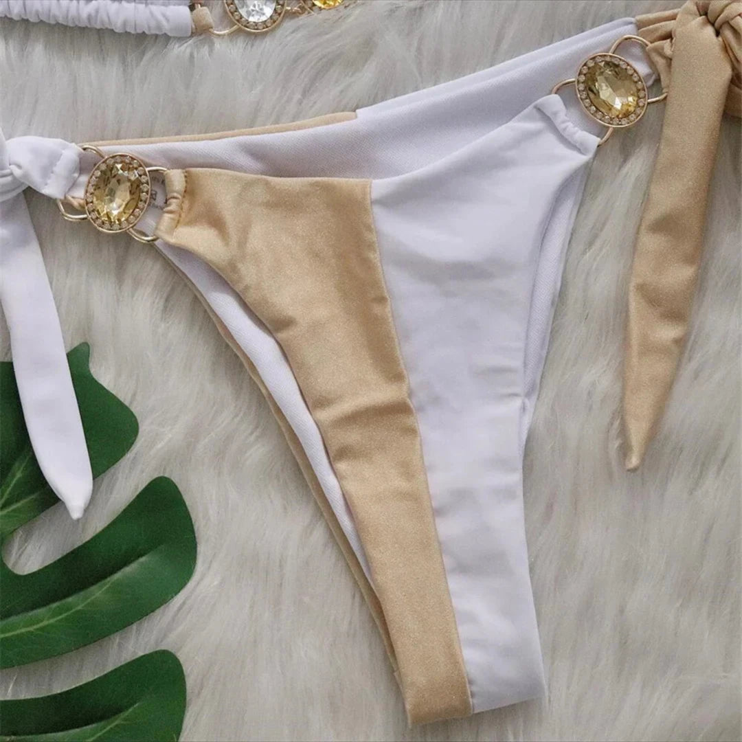 Gros plan sur le bas blanc et beige du bikini, anneau doré orné d'une pierre jaune sur la hanche et liens latéraux