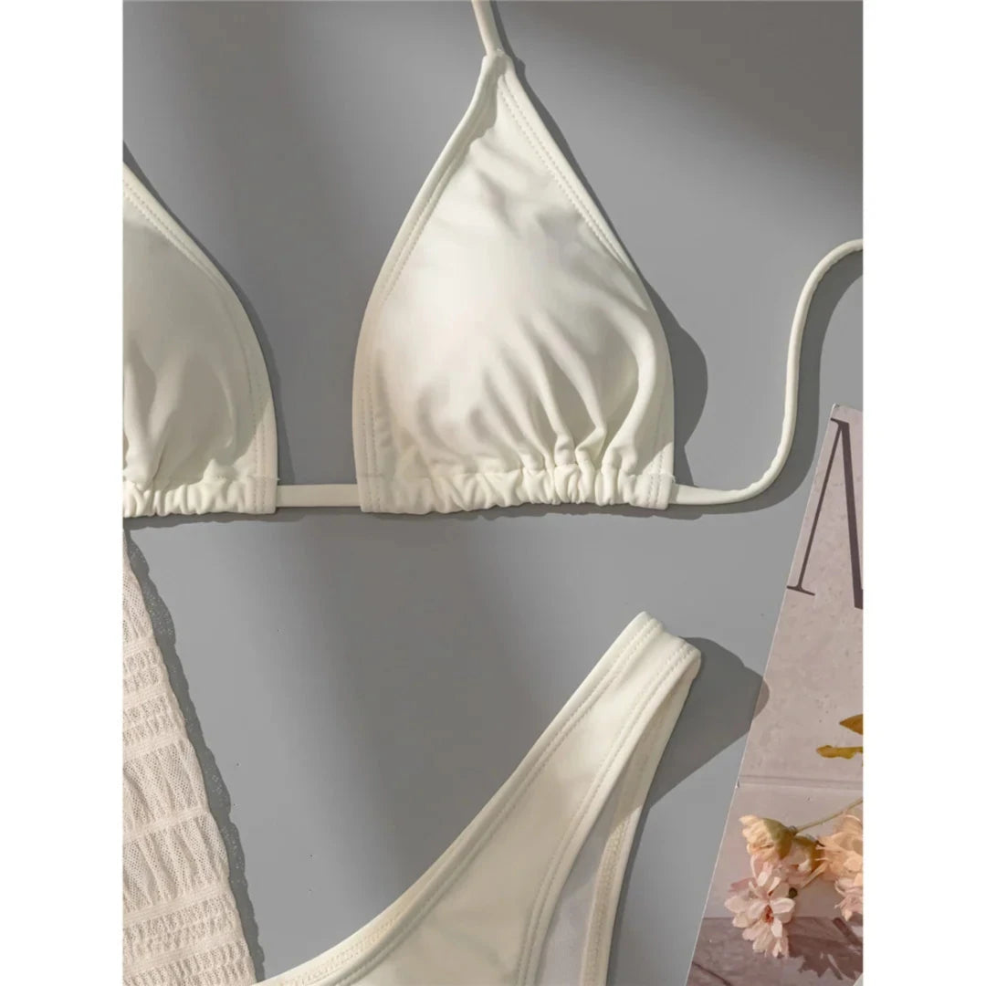 Gros plan sur le haut triangle crème à fins liens et le bas échancré du maillot beige, à côté d'un tissu texturé