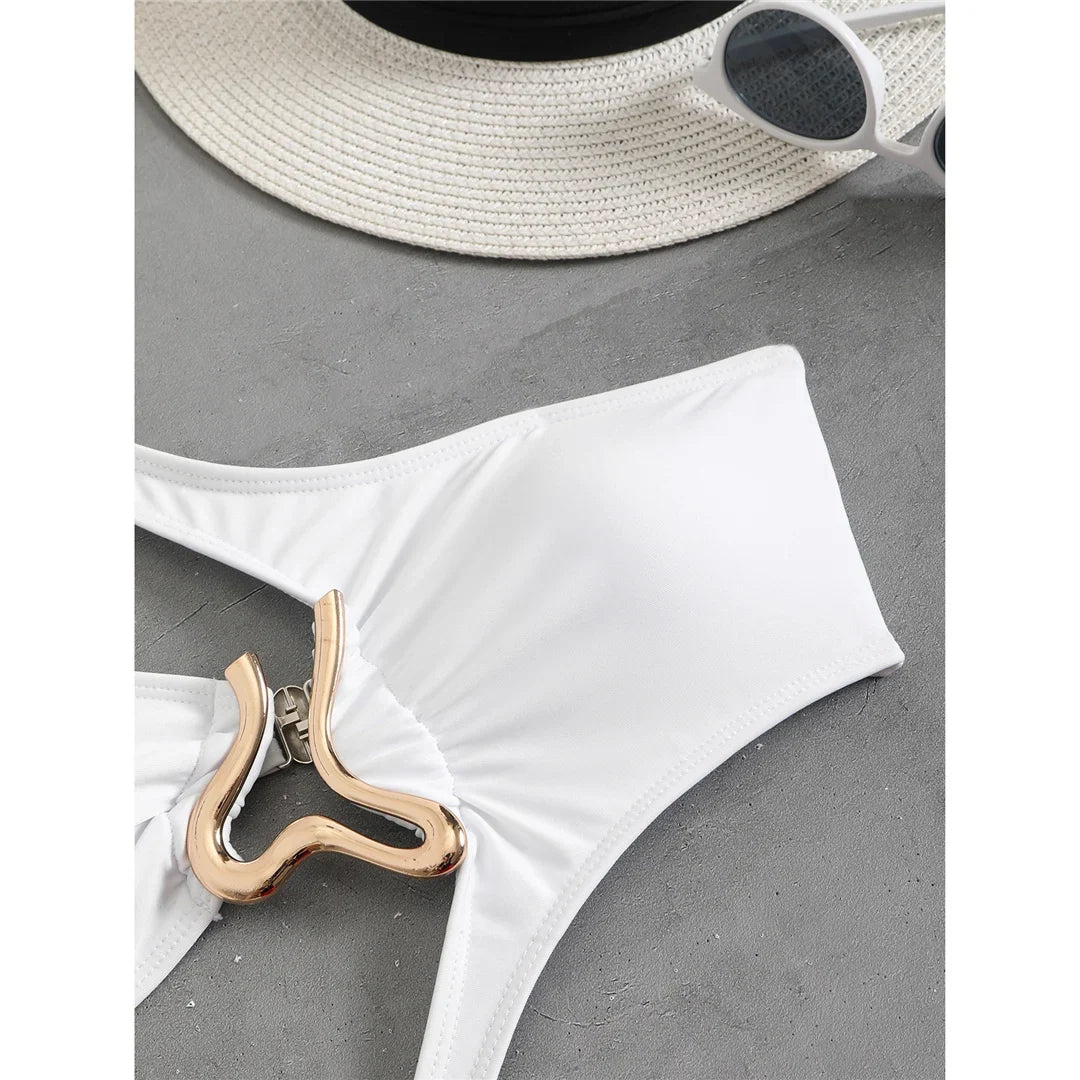 Gros plan sur le ventre du maillot blanc posé à plat, grand anneau doré et pli du tissu, chapeau et lunettes blancs en haut