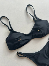 Gros plan sur le haut bikini string micro triangle noir à anneaux métalliques et bretelles fines sur fond clair