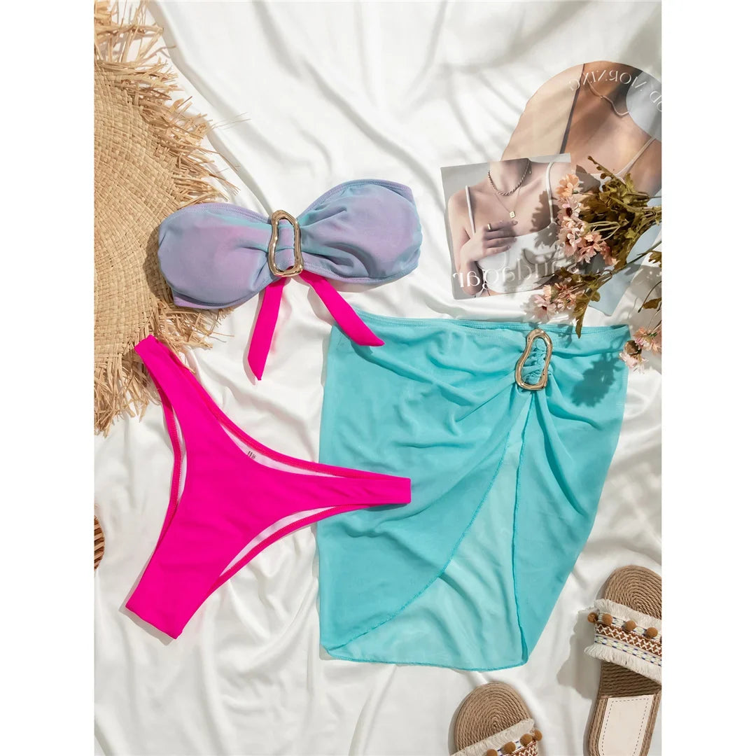 Maillot de bain trois pièces bandeau bleu lagon et rose avec jupe en voile posés à plat sur un drap blanc et un chapeau