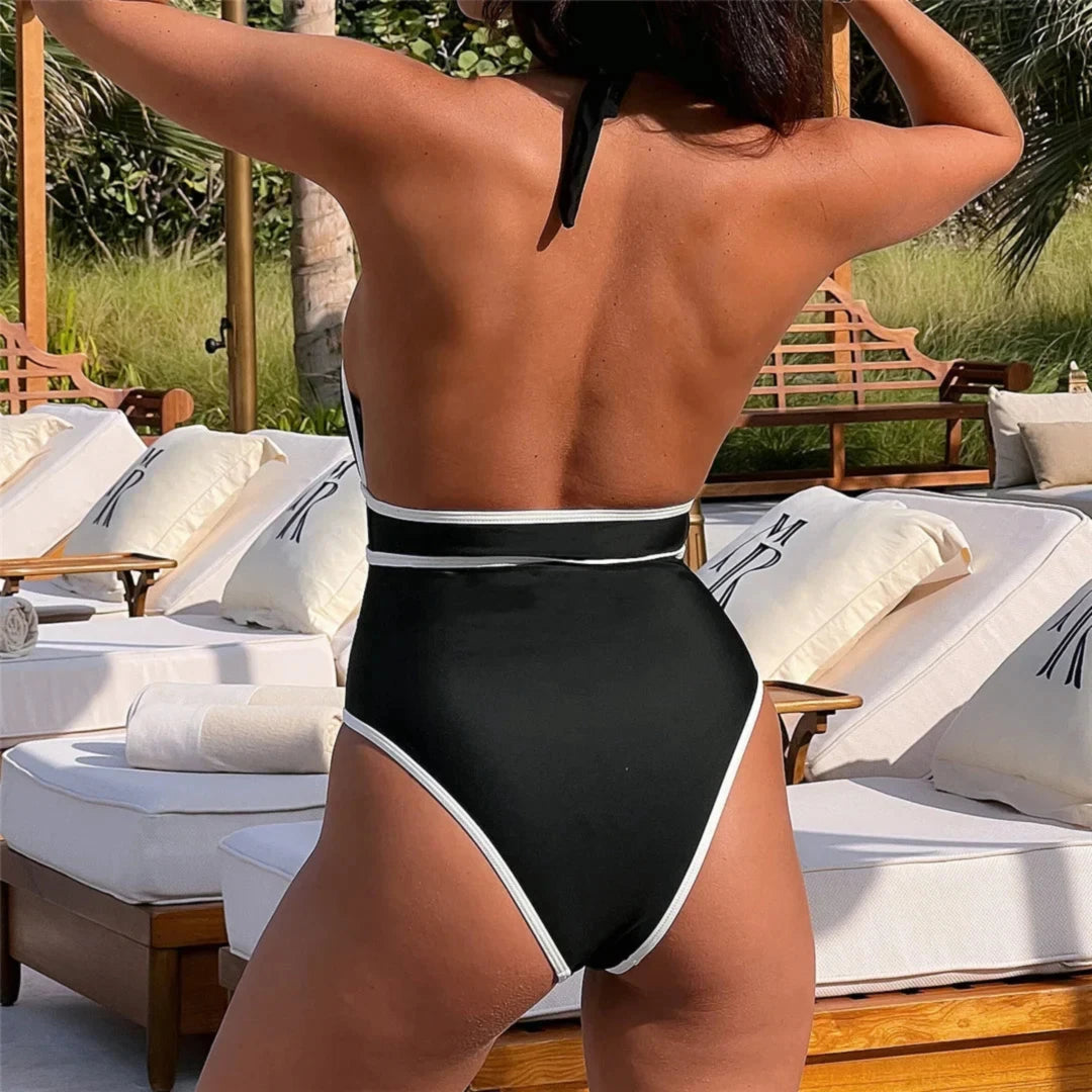 Maillot de bain une pièce tour de cou noir à liseré blanc vu de dos, dos nu et taille haute sur une chaise longue