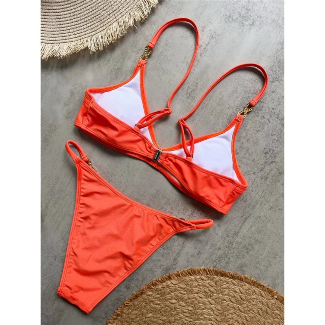 Bikini triangle orange vu de dos posé à plat sur un sol gris, doublure blanche et bretelles croisées aux anneaux strassés