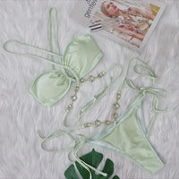 Bikini croisé sans armatures orné de strass vert clair posé à plat sur fond blanc, chaîne de pierres vertes et liens longs