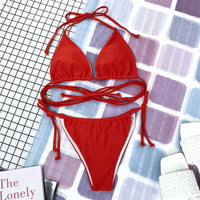 Bikini brésilien rouge étalé à plat sur un fond carrelé, avec un livre posé à côté et des lacets croisés