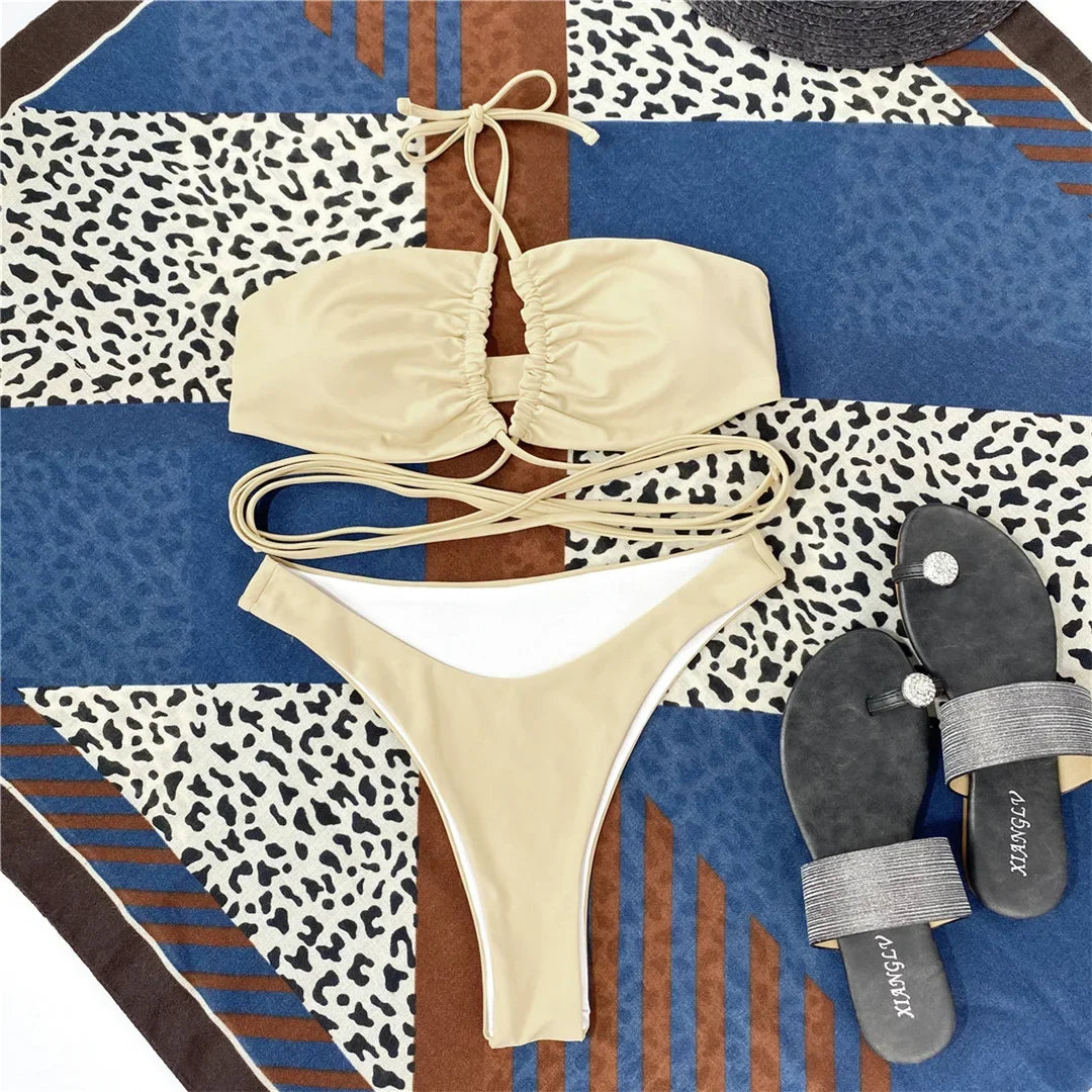 Bikini tour de cou à lacets croisés sans armatures beige posé à plat sur un foulard, avec sandales grises à côté