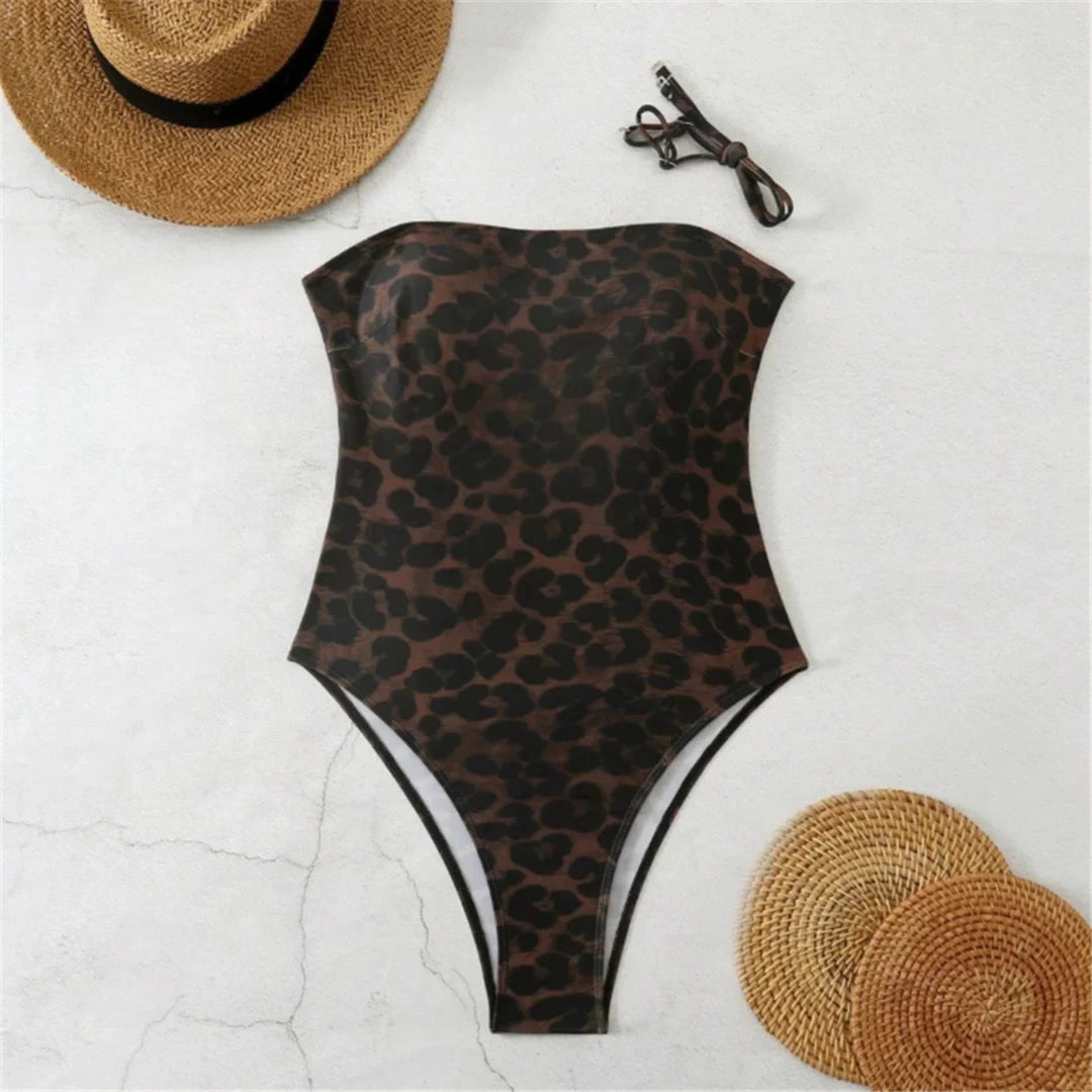 Maillot une pièce bandeau imprimé léopard posé à plat sur du marbre blanc, avec deux chapeaux de paille et des lunettes
