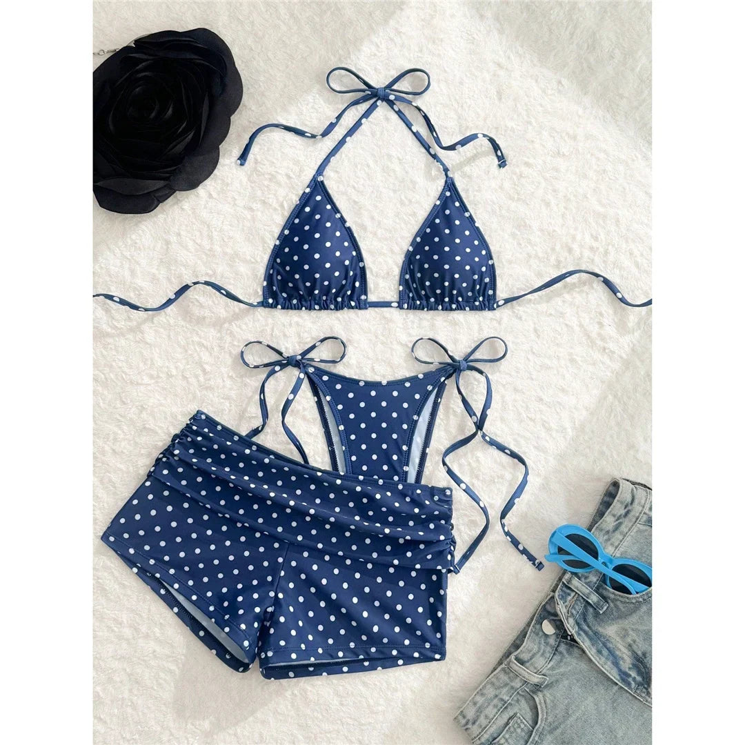 Maillot trois pièces à pois bleu foncé posé à plat sur une fourrure blanche, à côté d'un jean