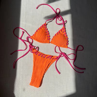 Bikini tour de cou rouge orangé posé à plat sur un tapis blanc, bordures festonnées et liens longs au soleil