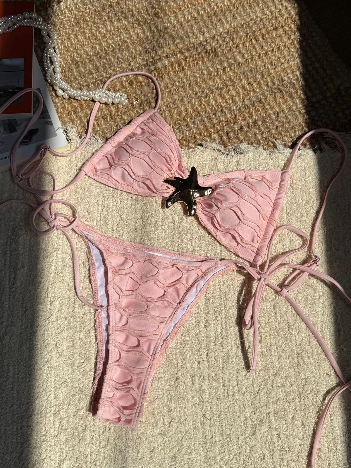 Bikini échancré à lanières et étoile métal beige rosé posé à plat sur un tapis et magazine, lanières fines