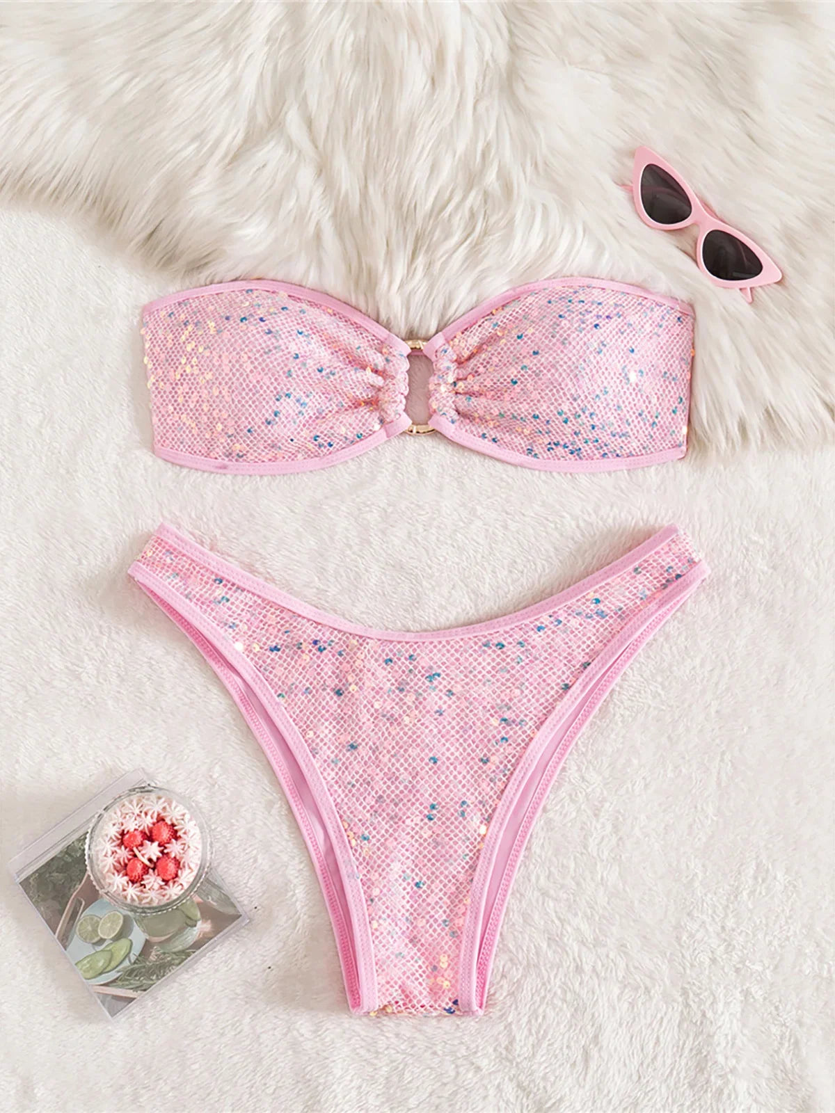 Bikini bandeau à sequins brillants taille basse rose à plat sur fourrure blanche, lunettes de soleil roses posées en haut
