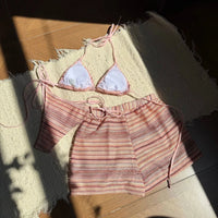 Haut triangle à doublure blanche et short rayé rose pêche posés à plat sur un tapis, lanières nouées