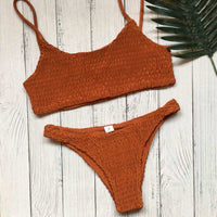 Bikini deux pièces texturé effet froissé orange à plat sur un parquet blanc, avec une feuille de palmier à côté