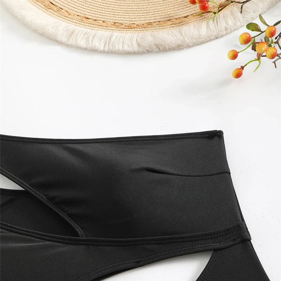 Gros plan sur la ceinture d'un maillot une pièce noir, bord croisé asymétrique sur fond blanc avec un chapeau