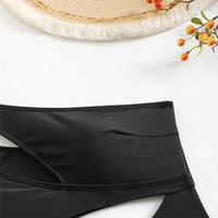 Gros plan sur la ceinture d'un maillot une pièce noir, bord croisé asymétrique sur fond blanc avec un chapeau