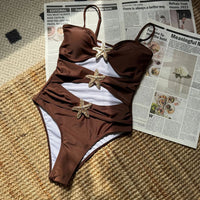 Monokini marron chocolat à découpes et étoiles de mer dorées, posé à plat sur un tapis en jute et un journal