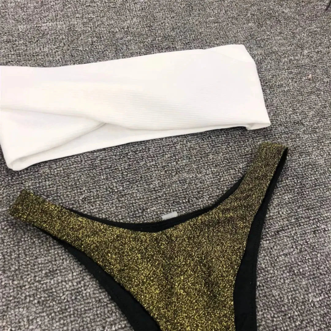 Gros plan sur le bas pailleté doré et le haut blanc torsadé d'un bikini bandeau scintillant posé à plat