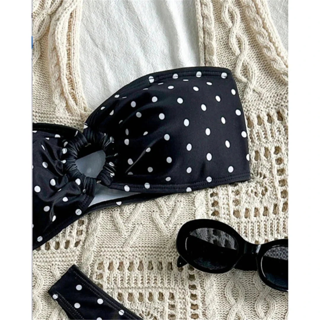 Gros plan sur le bandeau noir à pois blancs et son anneau central, posé sur un tissu crochet crème