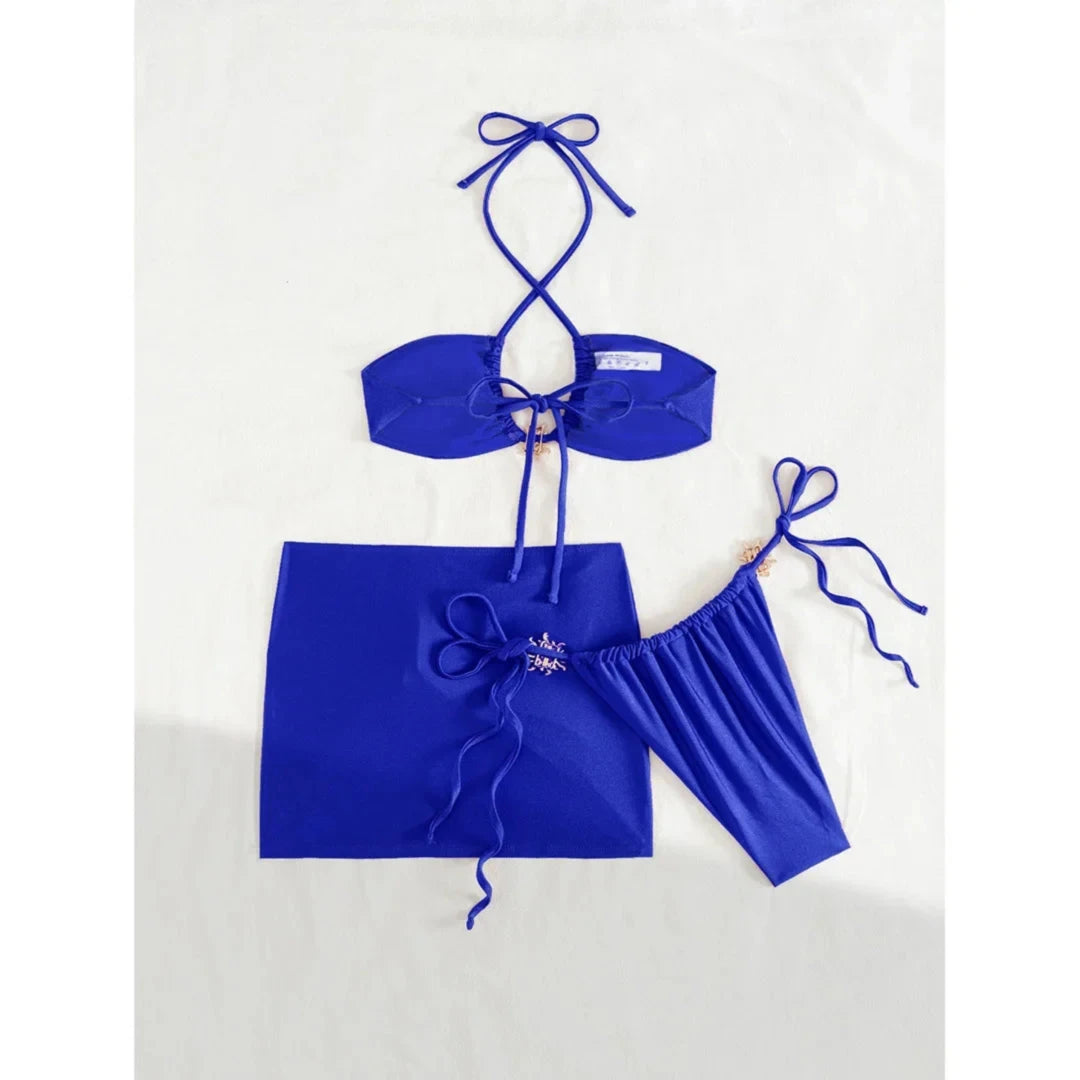 Maillot de bain trois pièces jupe halter à brides bleu disposé à plat, haut à bretelles croisées et jupe portefeuille ornée de métal