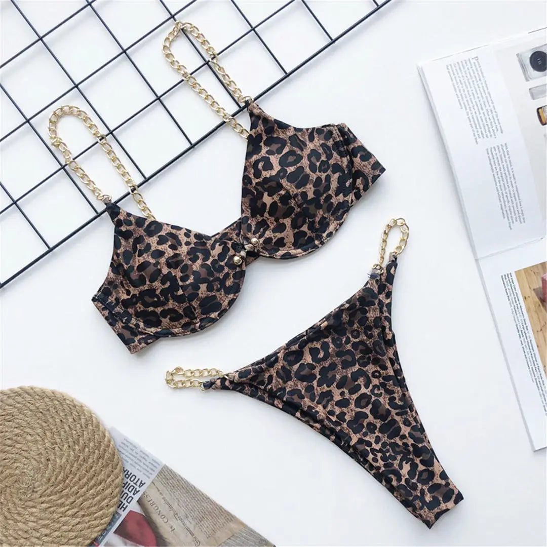 Bikini échancré à armatures avec chaîne dorée imprimé léopard posé à plat sur un tapis, armatures et chaînes dorées sur les bretelles