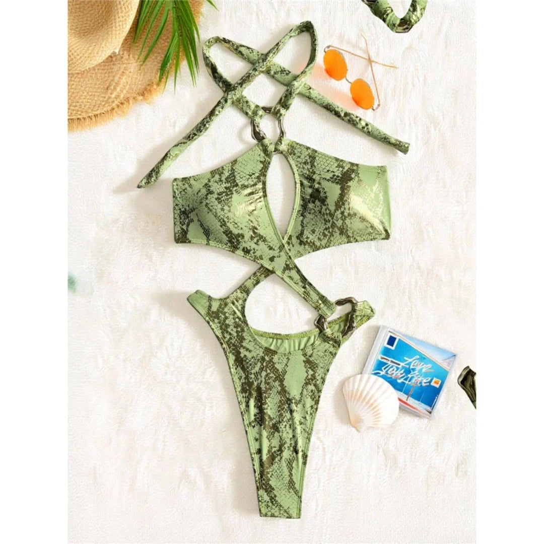 Maillot une pièce col halter vert et doré posé à plat, bretelles croisées au cou et lunettes orange et coquillage à côté