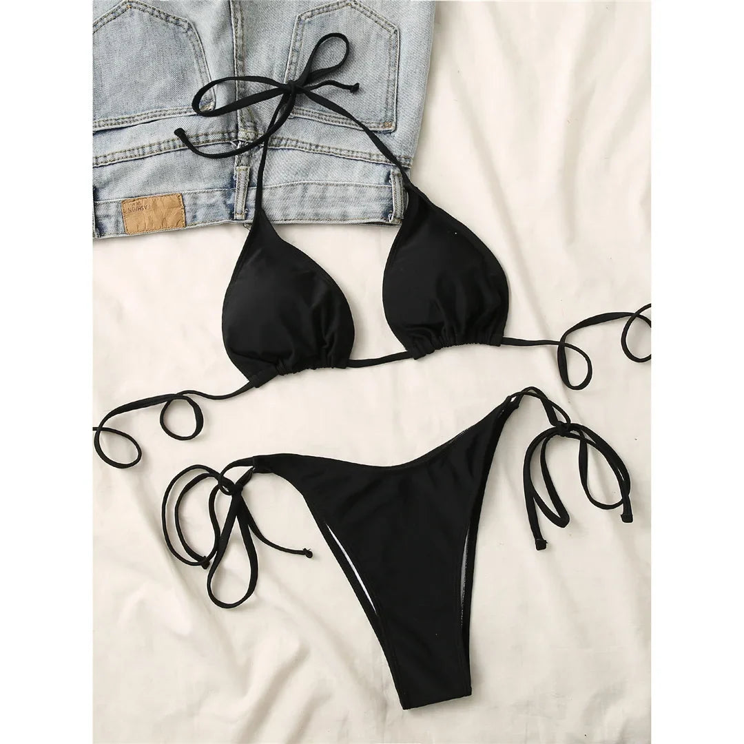Bikini brésilien tour de cou rembourré uni noir posé à plat sur une veste en jean, lacets longs étalés