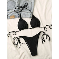 Bikini brésilien tour de cou rembourré uni noir posé à plat sur une veste en jean, lacets longs étalés