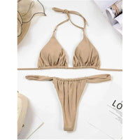Bikini string triangle froncé kaki posé à plat sur une table avec magazine, nœud sur la nuque et bas taille basse