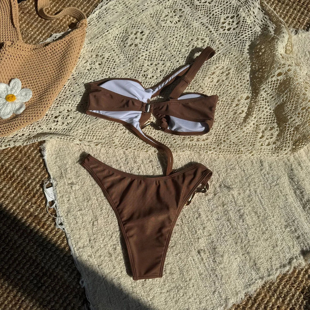 Maillot de bain marron café posé à plat sur un tapis crocheté, haut à bretelle asymétrique et bas coupé sur le côté