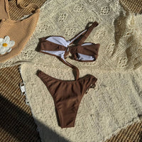 Maillot de bain marron café posé à plat sur un tapis crocheté, haut à bretelle asymétrique et bas coupé sur le côté