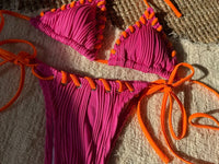 Gros plan sur le haut de bikini tour de cou rose vif bordé de cordons orange, brides longues au soleil