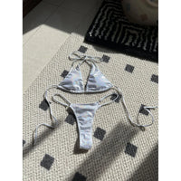 Bikini brillant scintillant triangle taille basse blanc posé à plat sur un tapis, liens longs et culotte fine