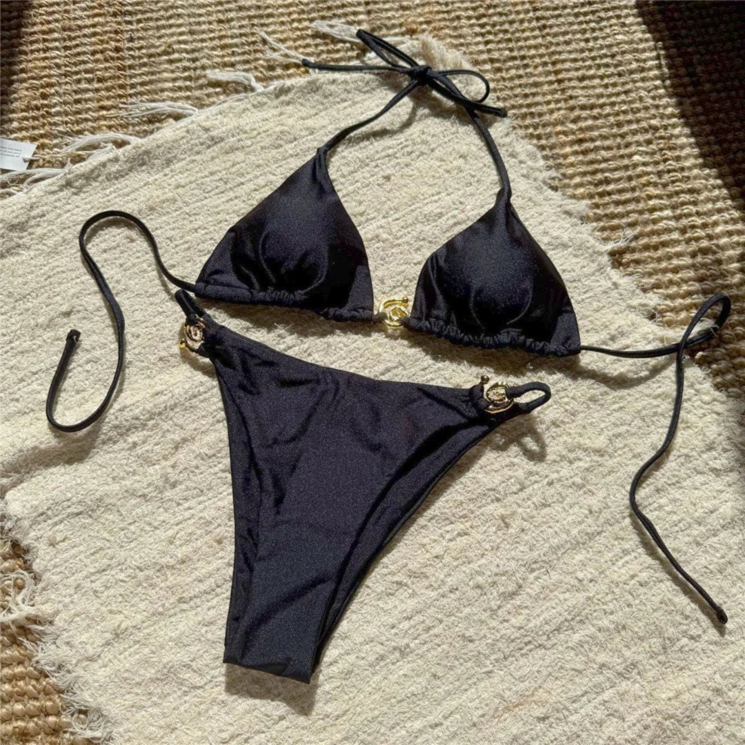 Bikini tour de cou à anneau métallique noir posé à plat sur un tapis clair, anneaux dorés au haut et au bas à côtés