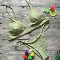 Bikini brésilien rembourré à taille basse vert kaki posé à plat sur du bois, agrumes et fleurs colorées autour